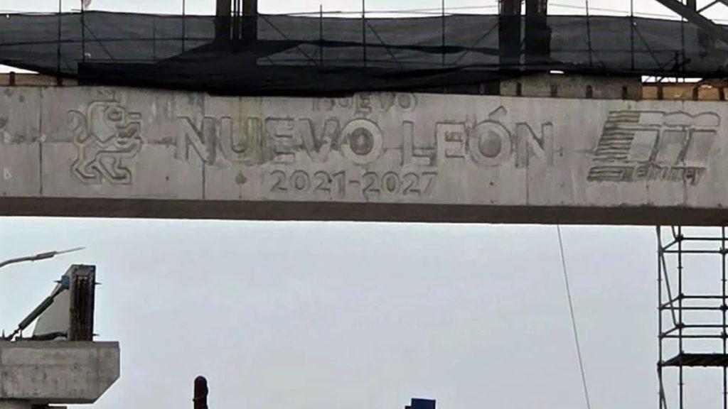Concrete Construction Beam with Graffiti Reading 'nuevo Leon 2021-2027', a Lion Emblem on the Left and a Logo on the Right, Scaffolding Above. - Especies Políticas