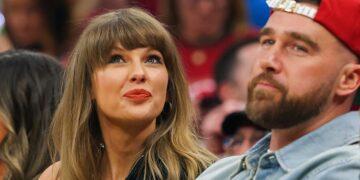 Woman with Long Light Brown Hair and Red Lipstick Looks Upward, Seated Beside a Bearded Man Wearing a Red Cap at a Crowded Event. - Especies Políticas