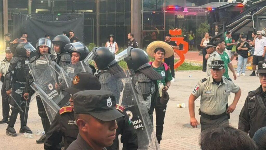 Riot Police in Full Protective Gear with Shields and Helmets Forming a Line in an Urban Plaza, Civilians Visible in the Background. - Especies Políticas