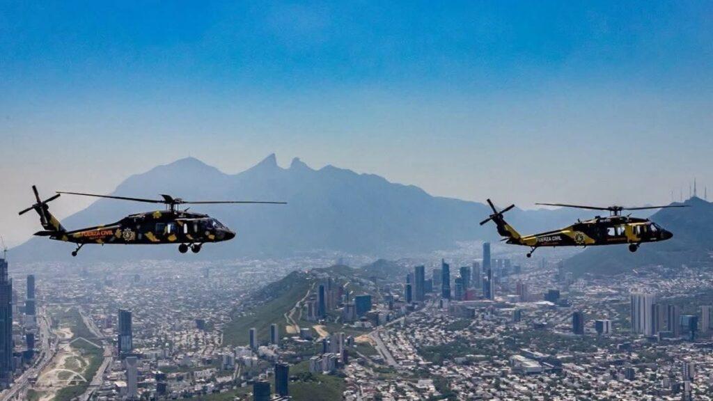 Two Black and Yellow Helicopters Fly in Formation over a Dense City with High-rise Buildings and a Mountain Range in the Distance. - Especies Políticas