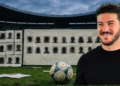 Personas-desaparecidas-en-nuevo-leon-durante-el-mundial - Especies Políticas Smiling Man in a Black Shirt Standing on a Soccer Field with a Blue-and-white Soccer Ball at His Feet; Behind Him is a Wall Covered with Silhouette Mugshots. - Especies Políticas