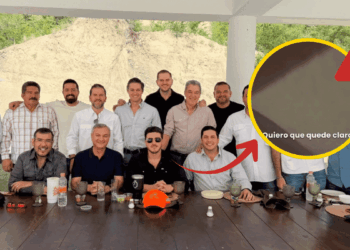 Group of men around a long outdoor table; a yellow circle highlights a zoomed area with a warning icon and the Spanish text 'Quiero que quede claro'.
