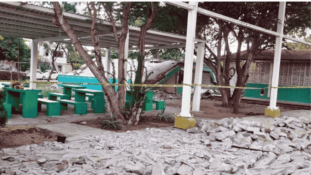Outdoor Seating Area with Green Benches and Tables, Trees, and Yellow Caution Tape Around a Damaged Shelter Area with Rubble on the Ground. - Especies Políticas